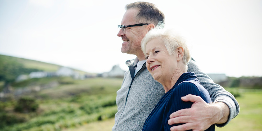 A smiling senior man with his arm around his wife.