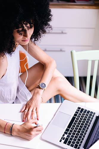 Young woman studying and taking notes while using her laptop.