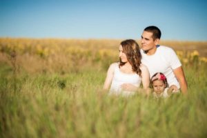 Father, mother, and toddler sitting outdoors in a field of tall grass and flowers.
