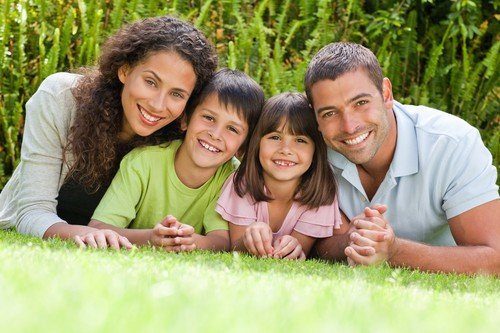 Family of four including a mom, dad, son, and daughter in the outdoors, laying on the grass and smiling at the camera because they have the most affordable life insurance policy possible.