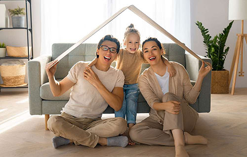 Young parents with a toddler holding a toy wooden house frame over their heads.