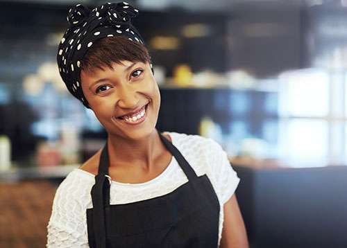 Black woman smiling as she welcomes you to her in her small business coffee shop.