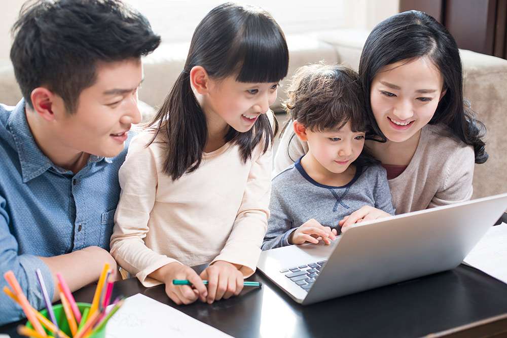 Asian family with mom, dad, and two kids leaning over a laptop looking for life insurance FAQs.