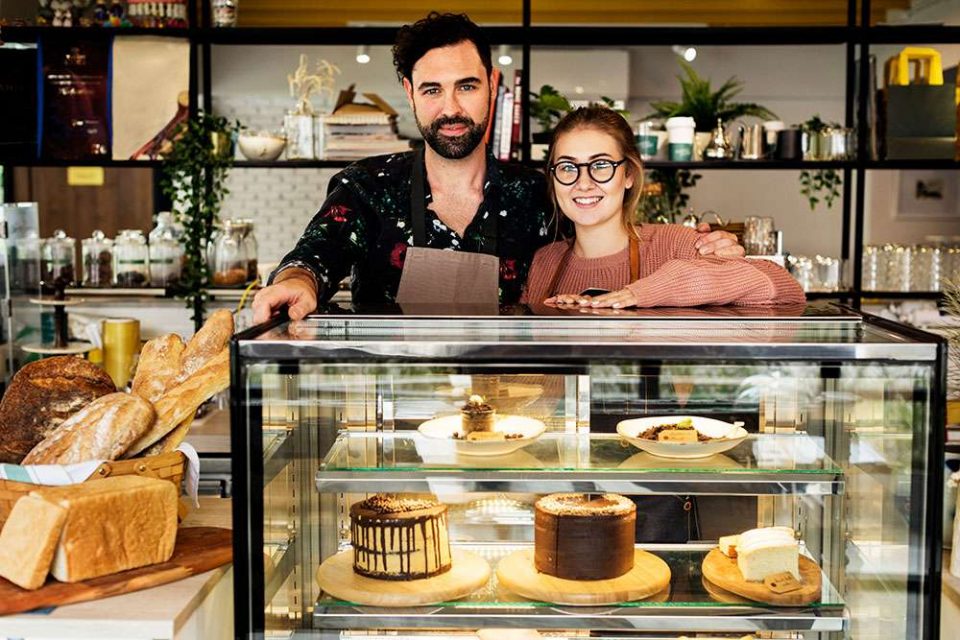 Man and woman behind bakery case in their bakery, smiling because they have small business life insurance.
