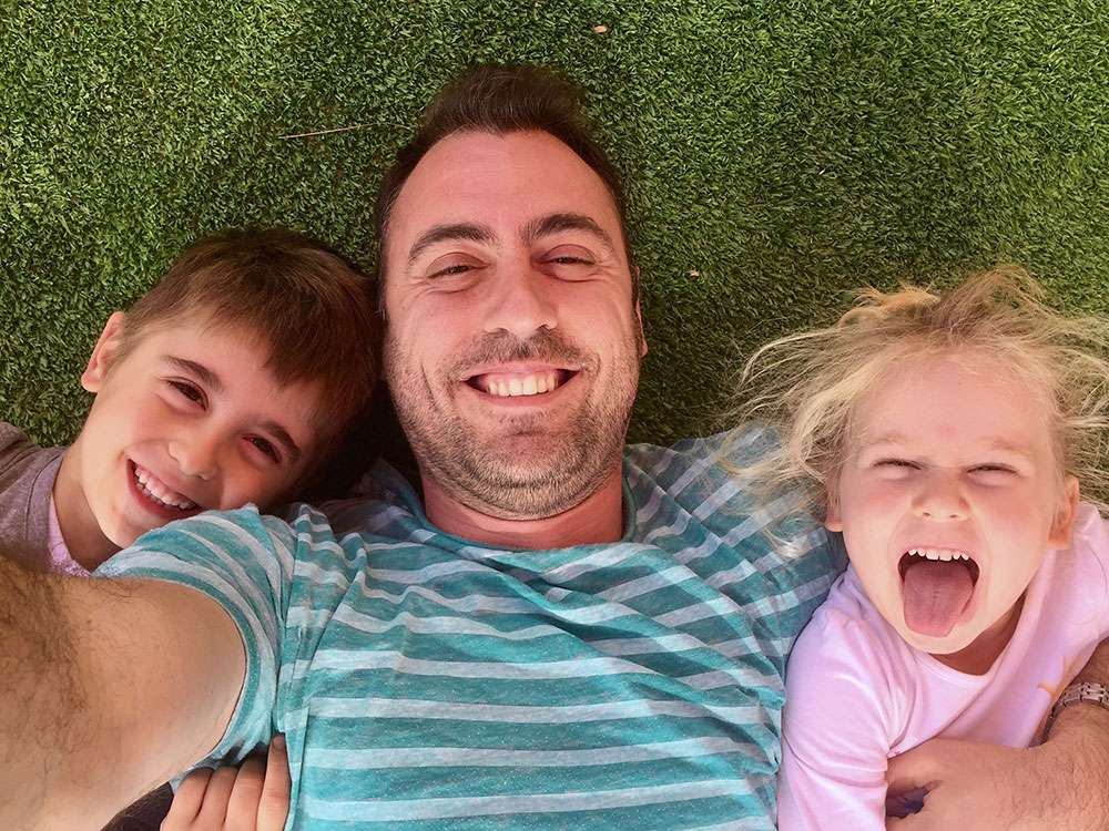 Laughing dad holding the camera above his head to take a picture of himself and his two kids, all smiling because they found the best term life insurance no medical exam with LifeQuote.