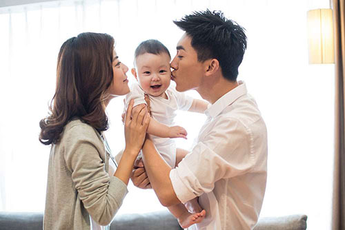 Asian couple holding their new baby. New parents are the perfect candidates for 20 year term life insurance quotes.