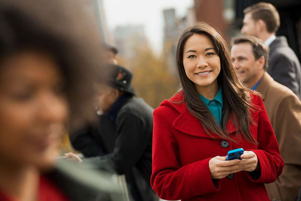 Asian woman in a red coat using her mobile phone to contact us via our LifeQuote email.