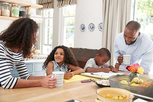 Black family having breakfast together in their kitchen, smiling because they looked into life insurance and types of life insurance.