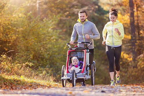 Mom and dad out jogging while pushing their baby in a stroller. Parents of young children are invited to get a 10 year term life insurance quote.