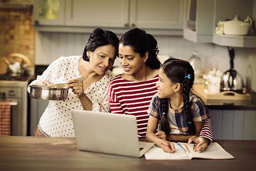 Mom, daughter, and granddaughter in the kitchen looking at a laptop.