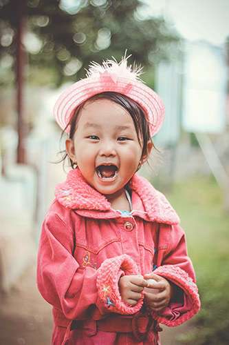 Adorable little girl wearing a pink hat and coat with a huge smile on her face.