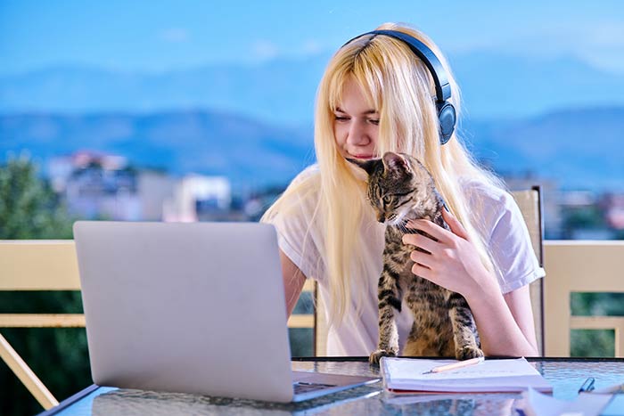 Una mujer joven con TDAH estudia con su computadora portátil mientras sostiene a su gato y usa auriculares