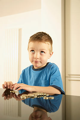 Little boy with a thoughtful expression sorting coins on a table.