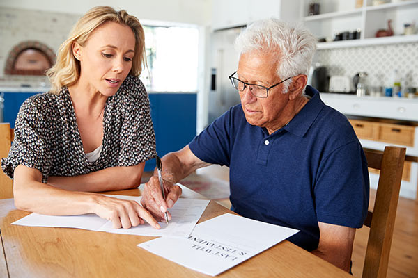 Woman sitting at the kitchen table with an older man as she helps him with his last will and testament