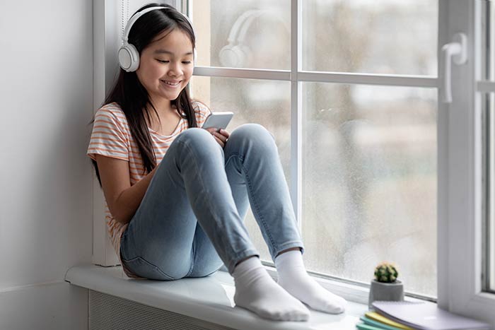 Young girl sitting in her room with headphones on, looking at content on her tablet