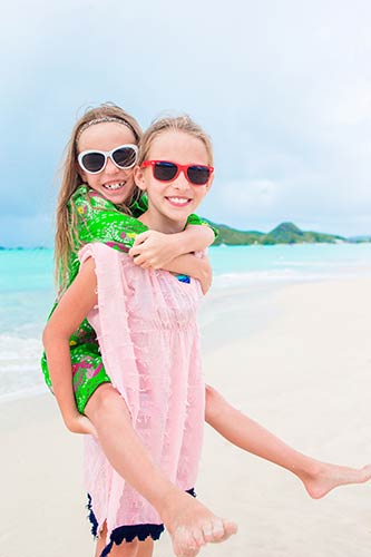 Two sisters playing on the beach, wearing bright sunglasses and smiling for the camera