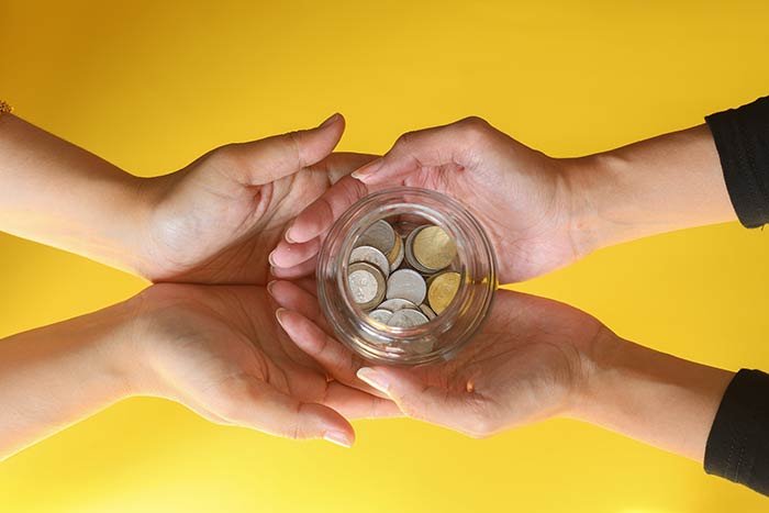 Hands holding a jar of coins, symbolizing the way permanent life insurance is an asset with a savings component