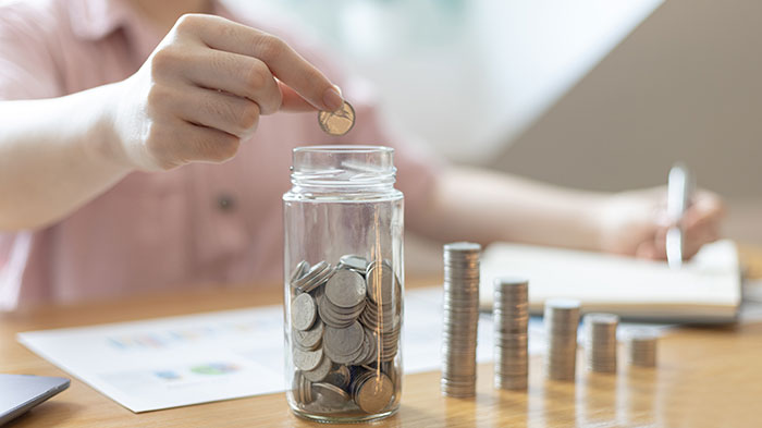 Close-up of a hand dropping coins into a jar, symbolizing the cash value savings component of universal life insurance