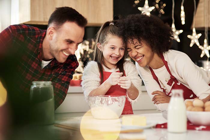 Father, mother and daughter laugh together in the kitchen while preparing a snack