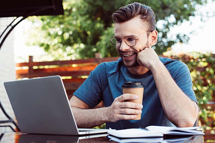 Man smiling at laptop while drinking coffee