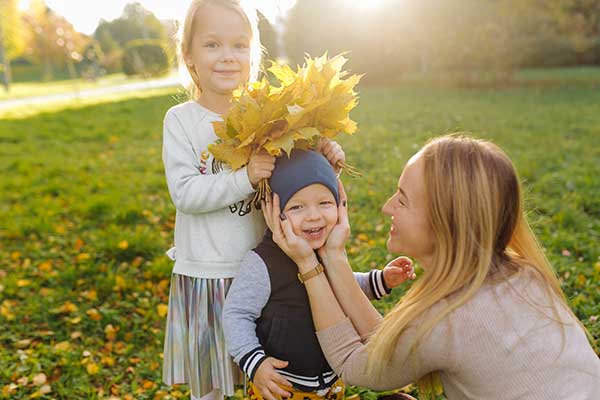 Mom with two kids playing in the park with autumn leaves