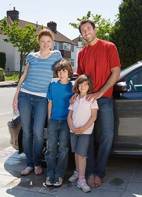 Family of four posing together next to their car
