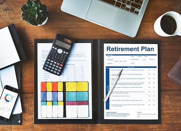Photo of a planner open on a desk with a retirement plan, pen, calculator, and financial charts