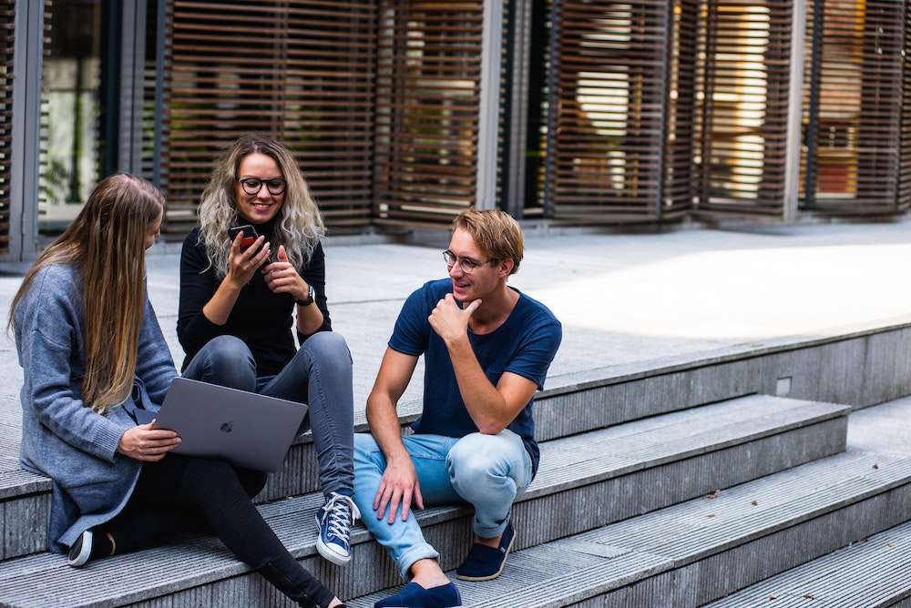 Three young people shop for life insurance quotes on a laptop and smartphone.