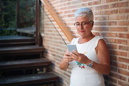 Senior woman wearing glasses looking up whole life insurance for seniors on her mobile phone.