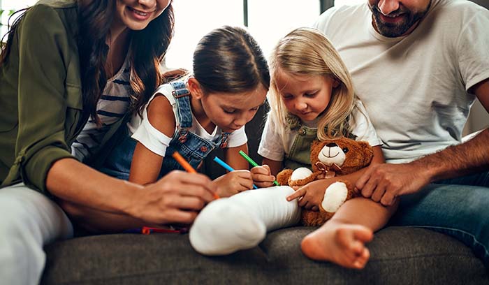 Family together on a couch laughing and signing their daughter's cast