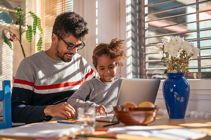 Father and daughter sitting at a kitchen table together using a laptop to research term life insurance