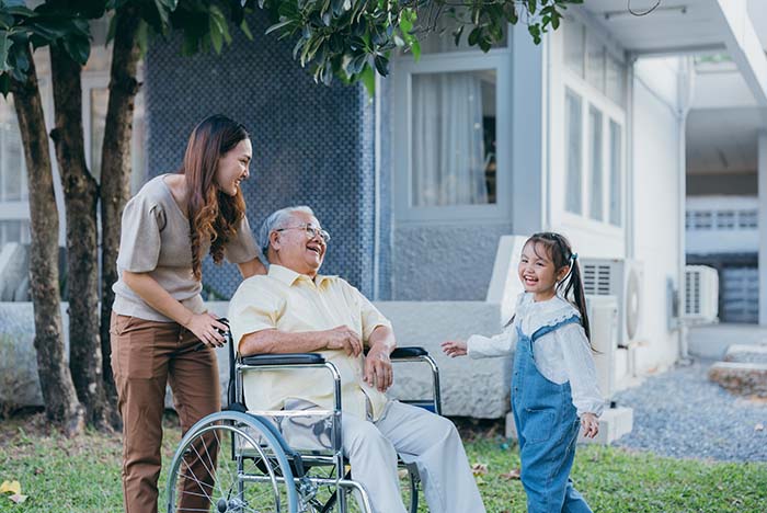 Mother and daughter visit and laugh together with grandfather in a wheelchair