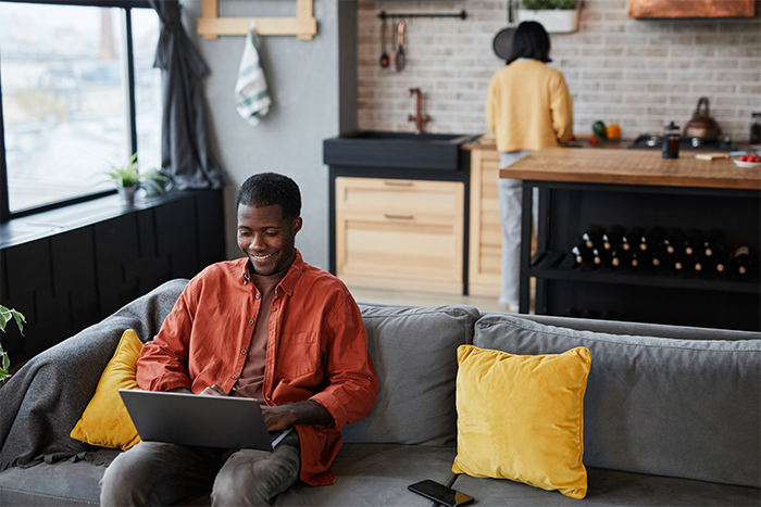 Man on couch with laptop explaining the benefits of converting term life insurance to permanent to his wife