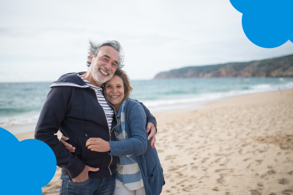 Smiling older couple embracing on the beach, considering whether to renew their term life insurance as they plan for the future together.